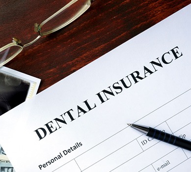 A dental insurance form set on a brown table next to glasses, X-rays, and dollar-bills