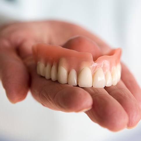 Close-up of hand holding a denture in San Antonio, TX