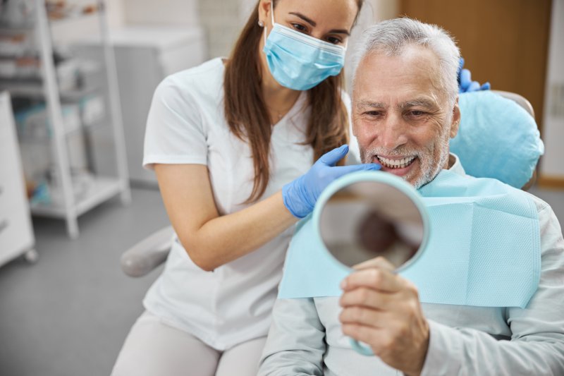 An older man admiring his new dental implant with a hand mirror